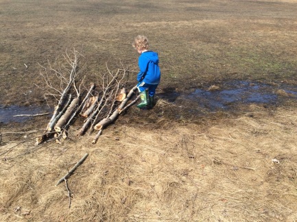 boy adding a stick to a bridge over a ditch