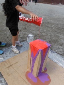 child pouring paint onto wooden tower